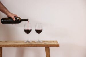 A person pours red wine into glasses on a rustic wooden table, elegant and simple.